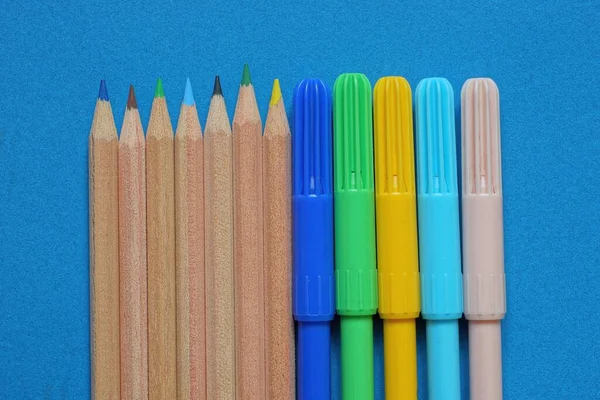 蓝色底色的一套褐色木制铅笔和彩色塑料记号 — 图库照片