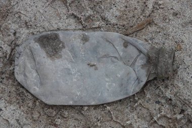Gri, eski, kirli bir plastik şişe sokakta yerde yatıyor.