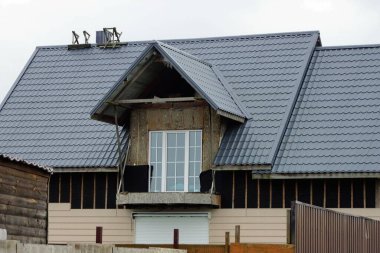 Gri özel bir evin ön cephesinde balkon ve çatısı kahverengi kiremitli bir çatı altında pencereler.