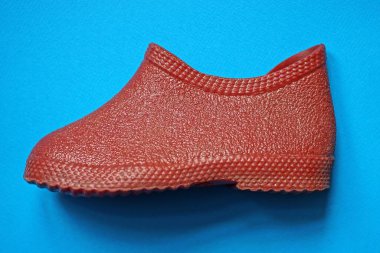 Kırmızı bir kauçuk ayakkabının küçük galoşları mavi bir masada yatıyor.