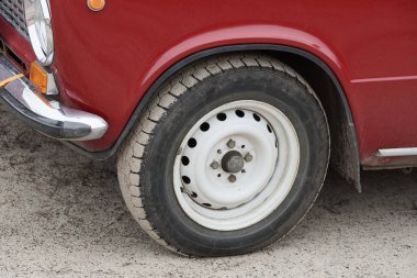 Kırmızı eski bir arabanın üzerindeki siyah beyaz tekerlek Gri bir kumun üzerinde duruyor