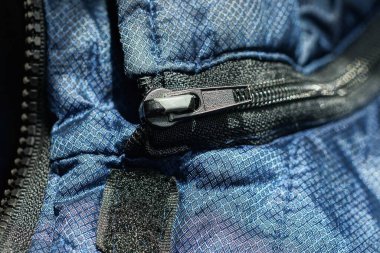 Mavi sentetik kumaşta siyah, kapalı, metalik bir fermuar.