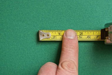 parmak yeşil bir masanın üzerinde sarı metal bir cetvel tutar.