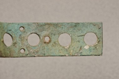 Gri arka planda yuvarlak delikleri olan eski, kirli, yeşil bir metal levhanın parçası.