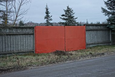 Kırmızı metal kapılar ve asfalt yolun yanındaki çimlerin arasındaki çitin beton gri duvarı.