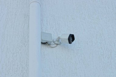 Caddedeki bir binanın gri beton duvarında asılı beyaz siyah bir güvenlik kamerası.