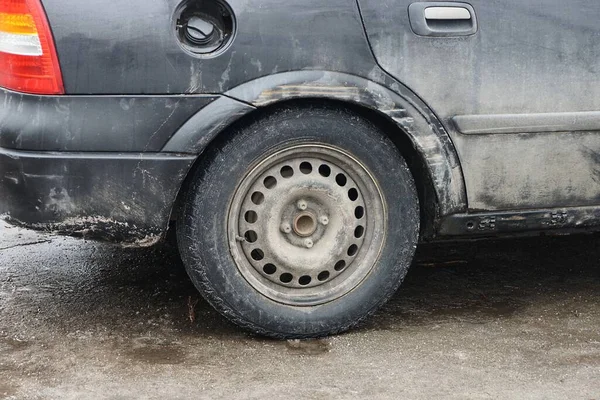 one black wheel on a dirty car of gray snow outside
