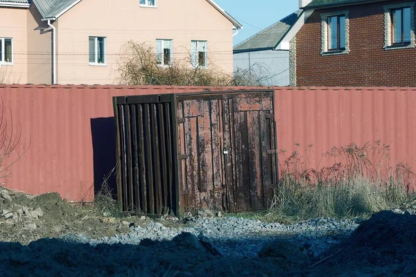 Pasla kaplı eski bir kahverengi demir kare konteynır sokakta çitin kırmızı metal duvarının yanında duruyor.