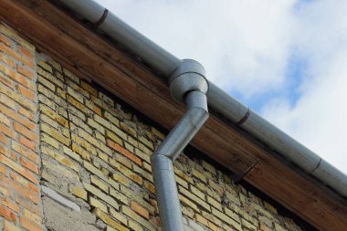 Kahverengi tuğla duvardaki gri metal drenaj borusu.
