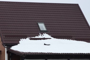 Bir kış caddesinde beyaz karın altında tek penceresi olan kahverengi kiremitli bir evin çatısına.