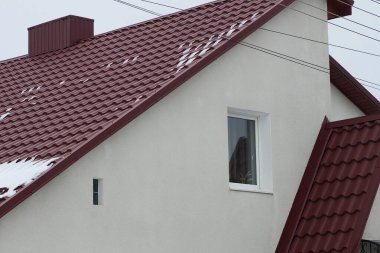 Beyaz tavan arası bir evin duvarı. Kış sokağında, kırmızı kiremitli bir çatının altında küçük bir pencere.