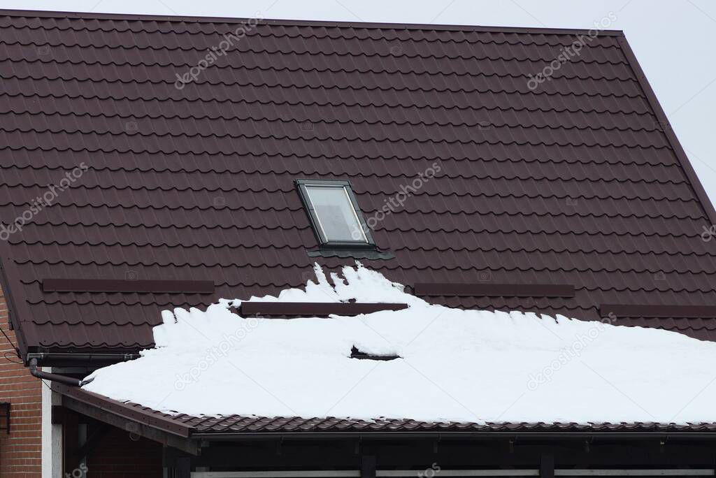brown tiled roof of a private house with one window under white snow on a winter street