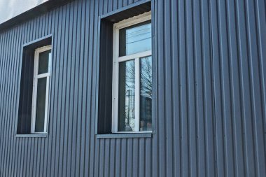 two white plastic windows on a black metal wall of a building on the street