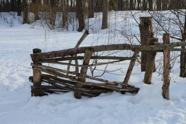 Gri kuru dallardan yapılmış eski bir kırsal çitin parçası ve kış sokağındaki kar yığınının içinde boş bir giriş. 