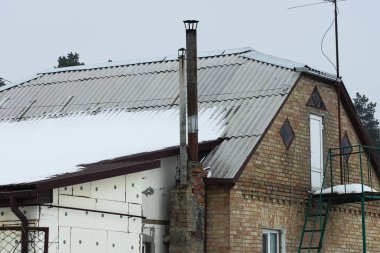 Kırsal bir evin gri tahta çatısındaki iki uzun baca. Kış sokağındaki beyaz kar altında.