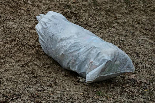 one large white plastic garbage bag lies on the gray ground outside