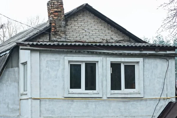 农村房屋灰色混凝土墙上的两扇窗户 屋顶上有砖头烟囱 — 图库照片