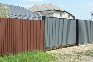 Büyük metal kapılar ve caddedeki gri kahverengi çitin bir kısmı.