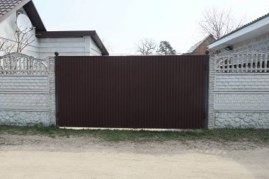 Büyük kapalı bir kahverengi metal kapı ve sokaktaki gri beton çitin bir parçası.