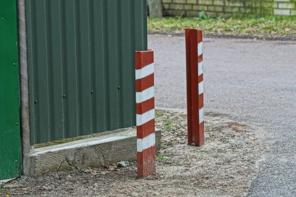 通りのフェンスの緑の金属壁の近くの道路脇の2本のストライプの鉄柵の柱 — ストック写真
