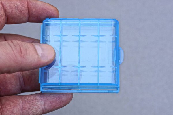 fingers on hand are holding blue plastic closed box on gray background