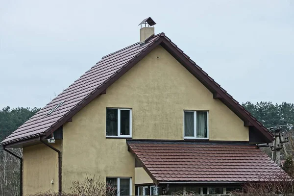 facade of a concrete private house under a brown tiled roof against a gray sky