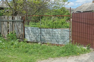 Gri eski metal kapılar ve ahşap tahtalardan yapılmış çitin bir kısmı ve yeşil çimlerin üzerinde kahverengi demir.