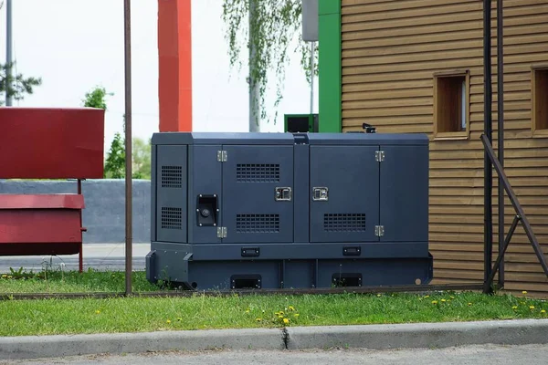 1台の黒い鉄の発電機が茶色の壁に向かって通りの緑の芝生に立っています — ストック写真
