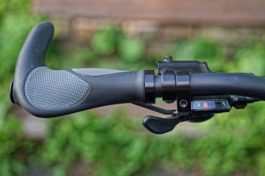 Siyah metal bir gidonun parçası. Plastik gri saplı ve fren kablosu yeşil arka planda.