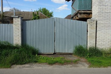 Gri metal kapılar ve yeşil çimlerin arasındaki tuğla çitin bir parçası.