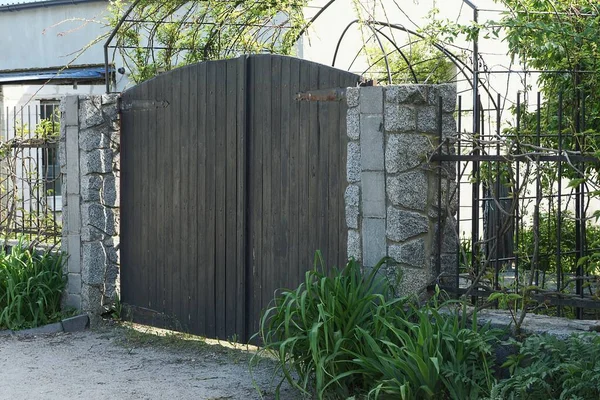 緑の芝生の外に黒い金属棒を持つ黒い木製の門と灰色の石のフェンス — ストック写真