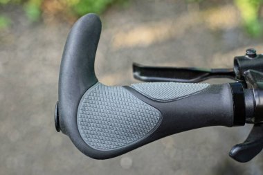 Siyah metal bir gidonun parçası. Plastik gri saplı ve frenli. Sokakta kablo var.