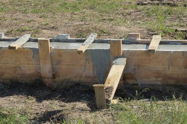 Gri beton ve ahşap kahverengi kalasların temelleri dışarıda yeşil çimlerde.