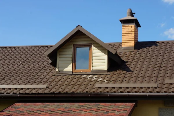 窓のある茶色の瓦屋根の下の民家の屋根裏部屋青い空に対するレンガの煙突 — ストック写真