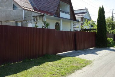 Kırsal bir sokakta büyük, kapalı bir kırmızı metal kapı ve duvar çiti