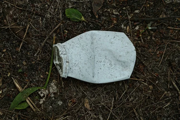 一个白色小塑料瓶里的垃圾躺在外面的黑土上 — 图库照片