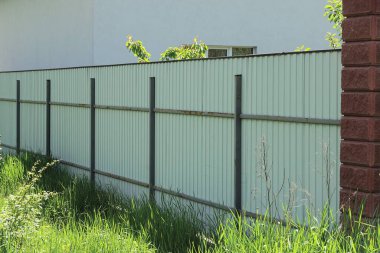 Sokakta yeşil çimlerde uzun gri çit duvar