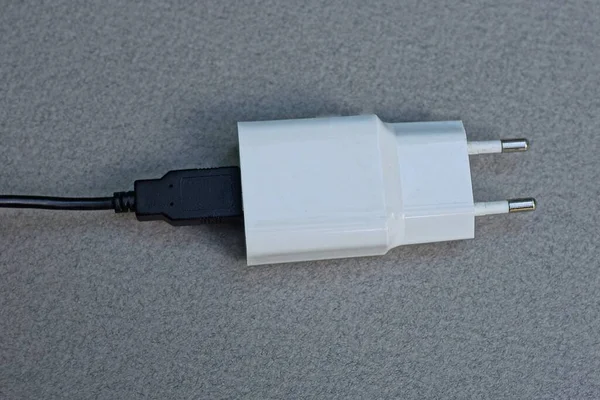 白色塑料适配器插座上装有Usb接口的黑色电缆躺在灰色桌子上 — 图库照片