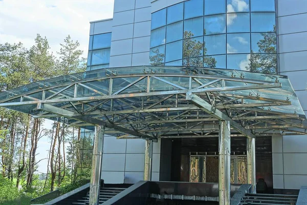 gray canopy cover made of metal and glass over black steps at the entrance of a large building made of square windows