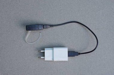 Tek kulaklıklı beyaz plastik prizde USB kablosu olan siyah elektrik kablosu gri bir masada yatıyor.