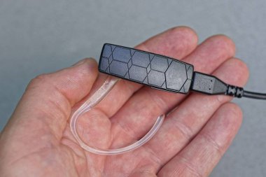 Gri arka planda, avuç içinde bir kablo bulunan büyük, siyah, siyah bir kulaklık.