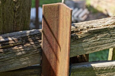 Metal bir köşeden gelen kahverengi demir paslı bir sütunun parçası. Sokakta gri tahta bir çit var.