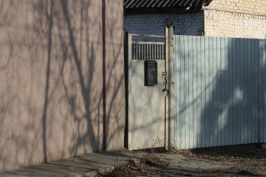 Posta kutusu olan gri metal bir kapı ve caddedeki binanın kahverengi beton duvarının yanında demir bir çit var.
