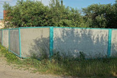 Kırsal bir sokakta, yeşil çimlerin üzerinde uzun gri beton bir duvarın parçası.