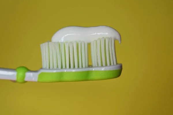 黄色の背景に白い歯磨き粉をつけたプラスチック製の歯ブラシ — ストック写真