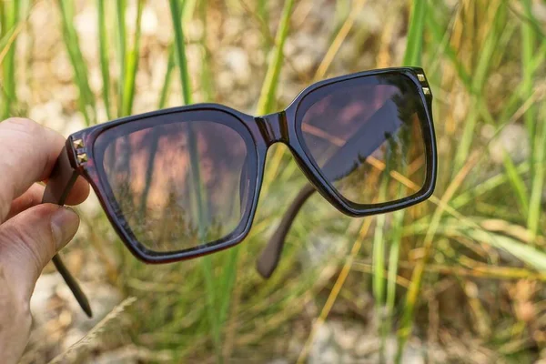 Finger Halten Braune Plastiksonnenbrillen Auf Einem Hintergrund Aus Grünem Gras — Stockfoto