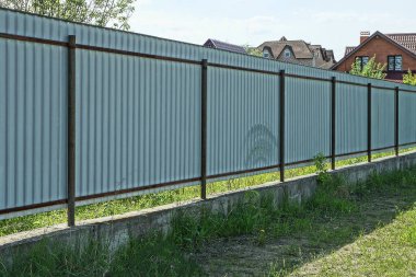 Sokakta yeşil çimlerde uzun gri çit duvar