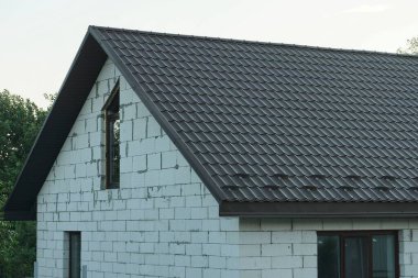 Kahverengi kiremitli çatının altında gri gökyüzüne bakan beyaz tuğlalı bir evin tavan arası.