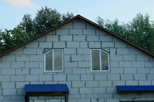 緑の木々と青空を背景に窓が2つある民家の白いレンガ造りの屋根裏部屋 — ストック写真