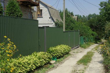 Kapalı kapılı yeşil uzun metal çit duvarlar ve caddelerde yaprakları olan bitkiler.